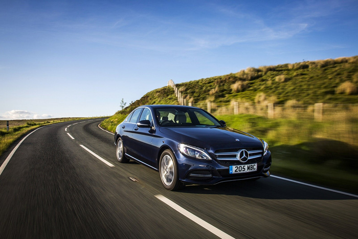 Dark blue Mercedes-Benz sedan driving on a winding road through green countryside under a clear blue sky, with UK licence plate reading 205 MBC, representing used cars and new cars.