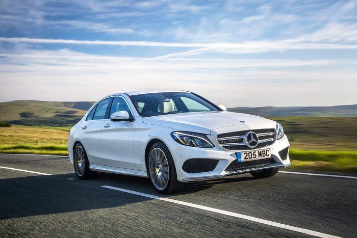 White Mercedes-Benz C-Class car driving on a countryside road with clear blue sky and green hills in the background, UK licence plate 205 MBC, representing new cars and used cars.