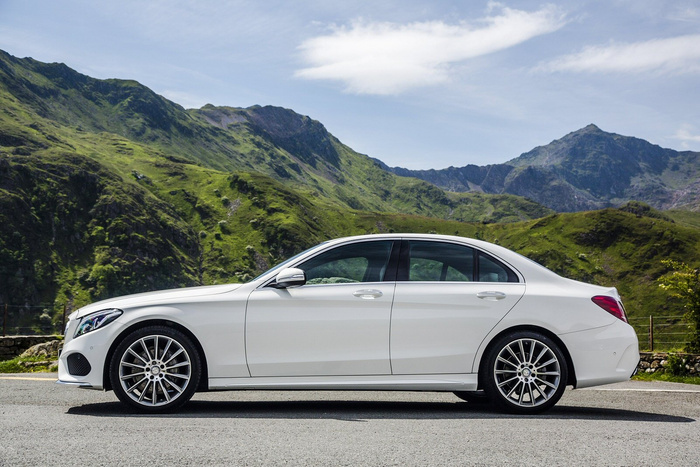 White luxury sedan parked on a paved road with green mountains and a blue sky in the background, showcasing a pristine exterior ideal for buyers interested in used cars or new cars.