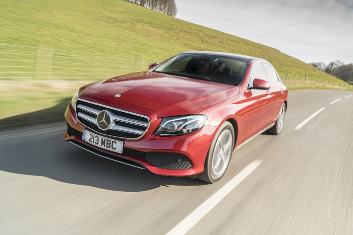Red Mercedes-Benz car with license plate 213 MBC driving on a countryside road with grassy hills in the background, showcasing a sleek luxury vehicle suitable for buyers interested in used cars and new cars.