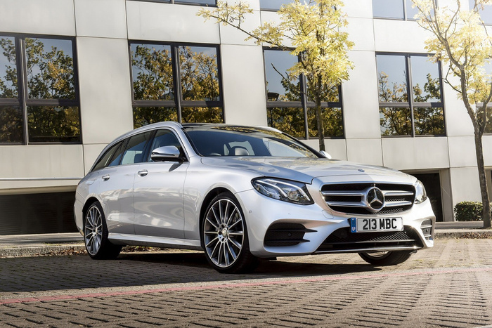 Silver Mercedes-Benz estate car with UK number plate 213 MBC parked on a paved area in front of a modern office building with reflective windows and trees with yellow leaves, illustrating a high-quality used car or new car.