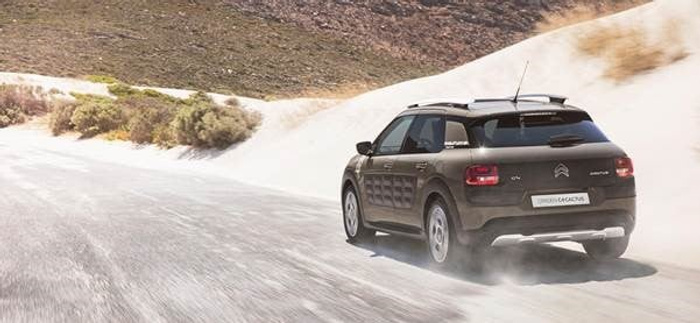 Brown Citroën C4 Cactus driving on a dusty mountain road with barren hills in the background, showcasing a modern compact SUV design, ideal for buyers interested in used cars and new cars.