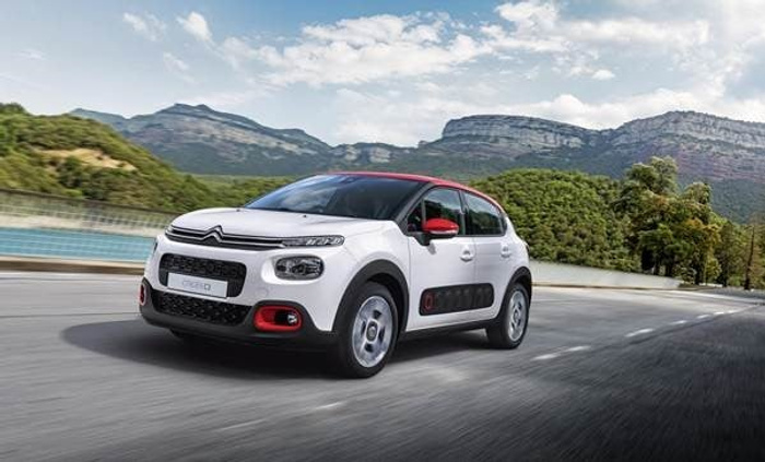 White Citroën C3 hatchback car with red accents driving on a scenic road with mountains and greenery in the background, representing a modern new car suitable for those looking to buy used cars or new cars.
