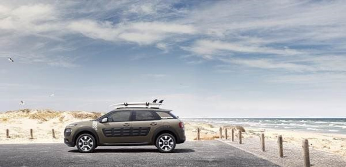 A green Citroën C4 Cactus car parked by a sandy beach with a partly cloudy sky. The car features distinctive airbump side panels and is positioned on a paved parking area near wooden posts and a sandy dune landscape. This image is ideal for advertising used cars or new cars in a coastal or outdoor setting.