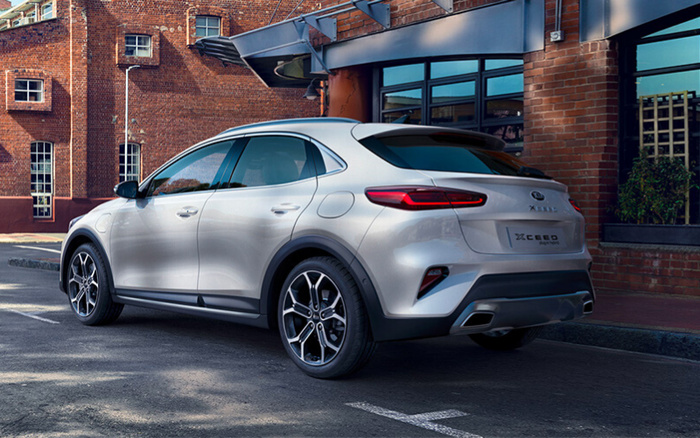 Silver Kia XCeed Plug-in Hybrid parked on a street with brick buildings and windows in the background, showcasing its sleek rear and side profile, representing options for new cars and used cars.