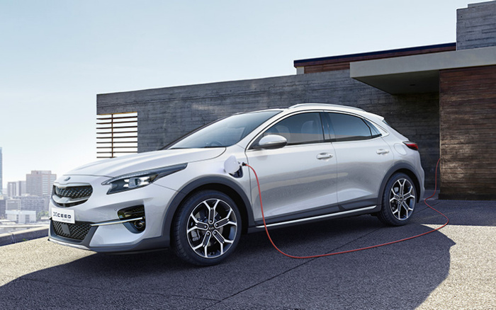 Silver Kia XCeed electric car charging outside a modern house with a cityscape in the background, showcasing a sleek design ideal for buyers interested in new cars and used cars.