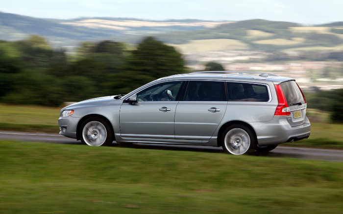 Silver Volvo estate car driving on a rural road with blurred green fields and distant hills in the background, illustrating used cars and new cars for sale.