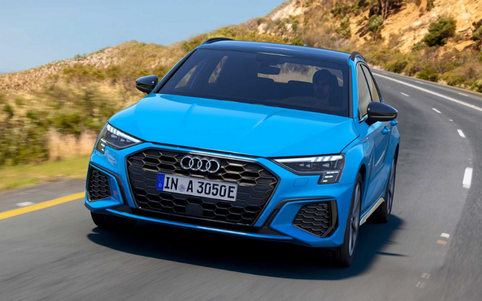 Blue Audi hatchback car with license plate IN A 3050E driving on a winding road with hills and vegetation in the background, representing new cars and used cars available for sale.