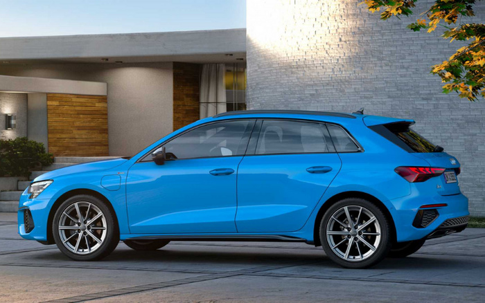 Side view of a blue Audi A3 Sportback electric car parked in front of a modern house with wooden and stone walls, showcasing sleek design with the Audi logo visible on the rear. Ideal image for used cars and new cars listings.