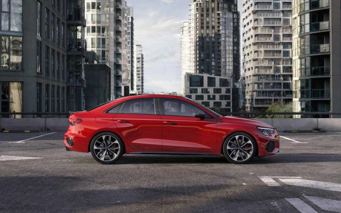 Side view of a sleek red sedan parked on a rooftop car park with modern high-rise buildings in the background, illustrating a stylish new car in an urban setting, suitable for used cars and new cars sales or advertisements.
