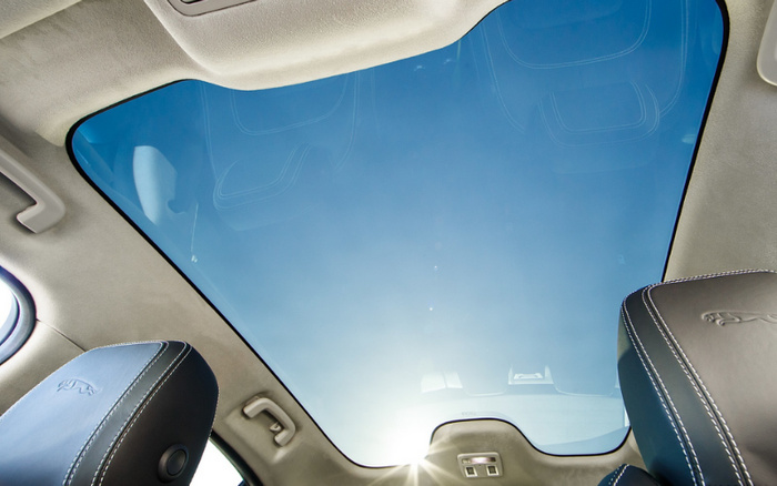 Panoramic sunroof view from inside a Jaguar car showing part of two black leather seats with Jaguar logos embossed, under a clear blue sky with sunlight shining through, highlighting the luxury interior of this vehicle ideal for buyers of used cars and new cars.
