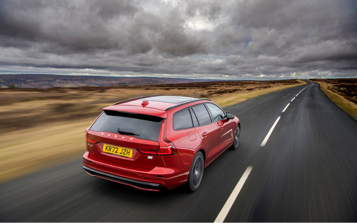 Red Volvo V60 estate car with registration plate KR72 JZH driving on a wet, empty rural road under a cloudy sky, ideal scene representing used cars and new cars on sale.