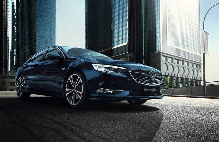 Stylish dark blue Vauxhall New Insignia car parked on a city street with tall modern glass buildings in the background, highlighting sleek design and sporty alloy wheels, representing attractive options for used cars and new cars in an urban setting.