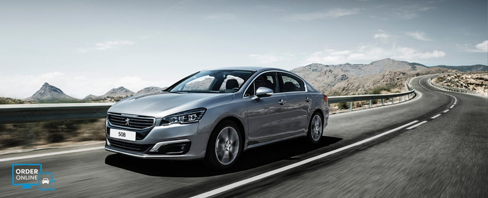 Silver Peugeot 508 sedan driving on a winding road in a mountainous area under a clear sky, with a licence plate reading '508'. In the bottom left corner, a blue icon with text 'ORDER ONLINE' and a car symbol, promoting online ordering. Image suitable for used cars and new cars advertisements.