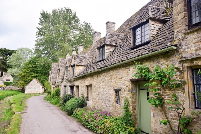 Row of traditional stone cottages with steeply pitched roofs and small dormer windows along a narrow country lane, surrounded by green vegetation and flowers, showcasing a picturesque rural scene unrelated to used cars or new cars.