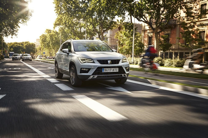 Silver Seat SUV driving on a sunlit urban street with trees and buildings in the background, showing front view with European license plate reading 9417 ATC, representing used cars and new cars on the road.