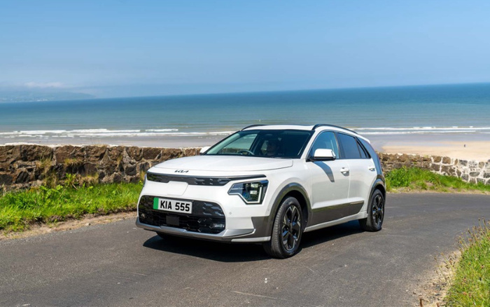 White Kia SUV with registration plate KIA 555 parked on a coastal road by a stone wall overlooking a sandy beach and calm sea, ideal for used cars and new cars buyers seeking scenic drives.