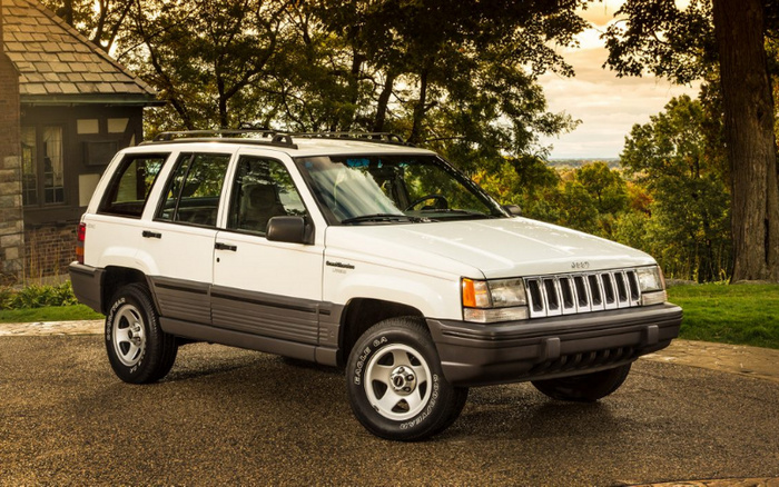 White Jeep Grand Cherokee Limited SUV parked on a driveway with greenery and a house in the background, showcasing a classic used car model. Ideal for those interested in used cars and new cars.