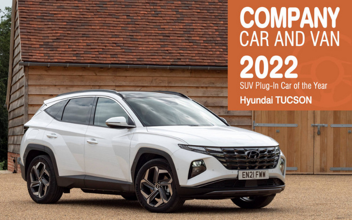 White Hyundai Tucson SUV parked in front of a wooden building with a tiled roof. Large orange banner on the right reads: 'Company Car and Van 2022 SUV Plug-In Car of the Year Hyundai Tucson.' Emphasises the vehicle as a top award-winning new car option, relevant for buyers interested in used cars and new cars.