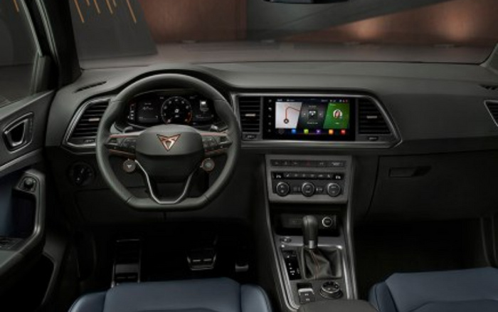 Interior view of a modern car dashboard featuring a multi-function steering wheel with a Cupra logo, a digital instrument cluster, and a central touchscreen displaying navigation and media options. The centre console includes climate control dials, gear shift, and various buttons, highlighting advanced features typical of used cars and new cars.
