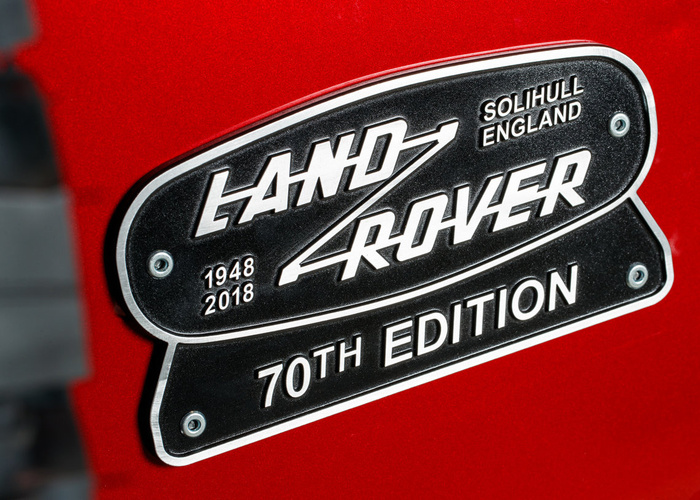 Close-up of a Land Rover badge on a red car commemorating the 70th edition from 1948 to 2018, with text 'Land Rover', 'Solihull England', and '70th Edition' visible on the black and silver emblem, related to used cars and new cars.