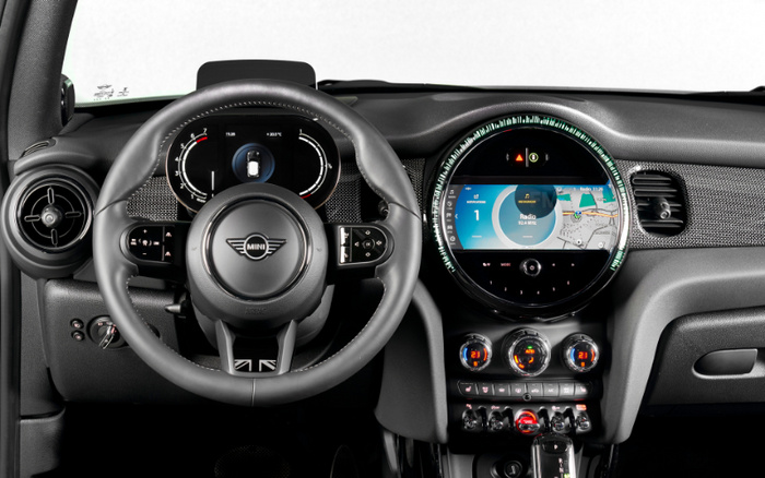 Interior dashboard of a Mini car showing the steering wheel with Mini logo, digital instrument cluster displaying speed and temperature, and a central circular infotainment screen featuring navigation map and radio settings. Climate control dials and toggle switches are visible below the screen, highlighting modern technology and design suitable for both used cars and new cars buyers.