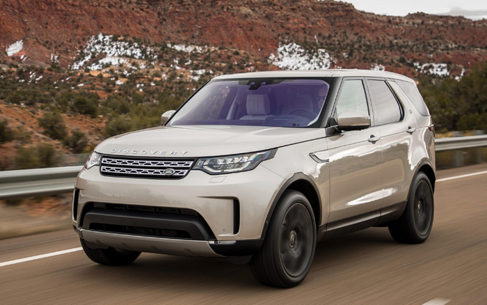 Silver Land Rover Discovery SUV driving on a road with rocky hills and sparse vegetation in the background, showcasing a modern and sleek design, suitable for buyers searching for new cars or used cars.