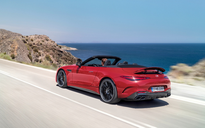 Red convertible sports car driving along a coastal road with cliffs and ocean in the background, showcasing a sleek design and modern features ideal for enthusiasts looking for new cars or used cars with high performance and style.