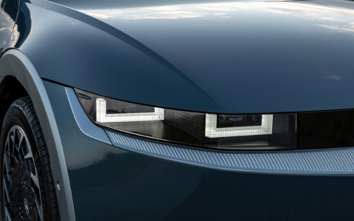 Close-up of a dark blue car's front headlight with distinctive angular LED daytime running lights, showcasing modern design and detailing, suitable for promoting used cars and new cars.