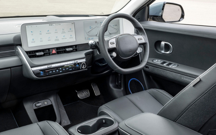 Interior view of a modern car featuring a sleek dashboard with dual digital displays showing navigation, media, and vehicle information. The steering wheel includes integrated controls, and the centre console has climate control settings. The design highlights black leather seats and a clean, minimalist layout, ideal for used cars and new cars buyers seeking advanced technology and comfort.