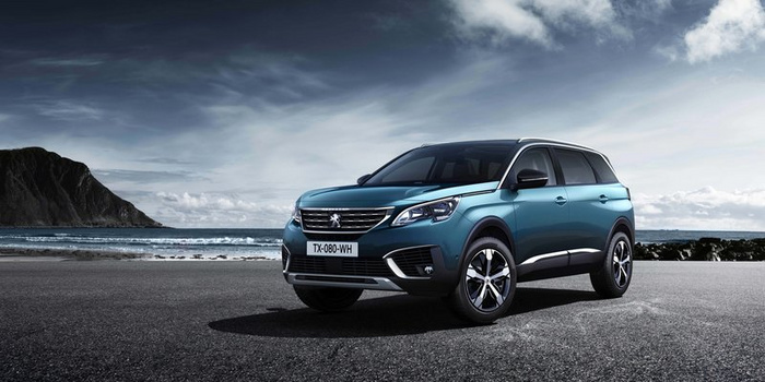 Blue Peugeot SUV parked on an empty coastal road with rocky cliffs and the sea in the background under a cloudy sky, showcasing a modern front grille and headlights, emphasising used cars and new cars.