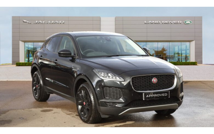 Black Jaguar SUV parked in front of a Jaguar and Land Rover dealership with signage visible. The car has a license plate showing the word 'APPROVED,' indicating it is a certified used car. The image highlights both new cars and used cars available at the dealership.