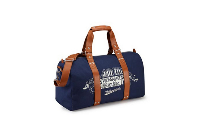 Navy blue and brown leather weekend duffle bag featuring white printed design of a Volkswagen Transporter van with text 'Volkswagen Kamiker', '2.3 million one version', 'delivery performance', and 'Volkswagen' on it, isolated on white background. Ideal for used cars and new cars enthusiasts.