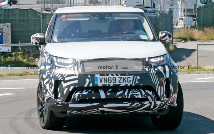 Front view of a camouflaged prototype car with UK registration plate VN69 ZKG driving on a road, featuring black and white striped test wraps on the front bumper and lower grille area, LED headlights, and a white hood, representing a new car model possibly undergoing testing, relevant for used cars and new cars market.