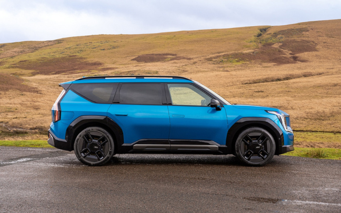 Side view of a blue modern SUV parked on a wet road against a backdrop of rolling brown hills under a cloudy sky, showcasing a sleek design ideal for both used cars and new cars markets.