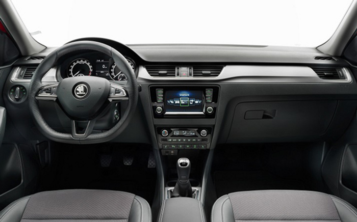 Interior view of a modern car showing the dashboard, steering wheel with Škoda logo, digital instrument cluster, central touchscreen displaying navigation and media controls, manual gear stick, air conditioning controls, and front seats. This image highlights features relevant for buyers considering used cars or new cars.
