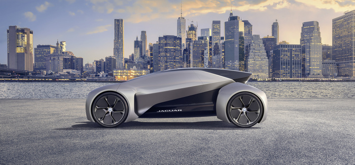 Silver futuristic Jaguar concept car with sleek aerodynamic design and large black wheels parked on waterfront with a city skyline in the background at sunset, highlighting innovative design trends in used cars and new cars.