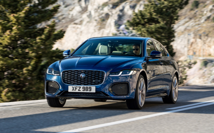 Blue Jaguar XF luxury sedan with registration plate XFZ 989 driving on a mountain road with rocky cliffs and trees in the background, showcasing sleek design and modern headlights, ideal for shoppers searching for used cars and new cars.