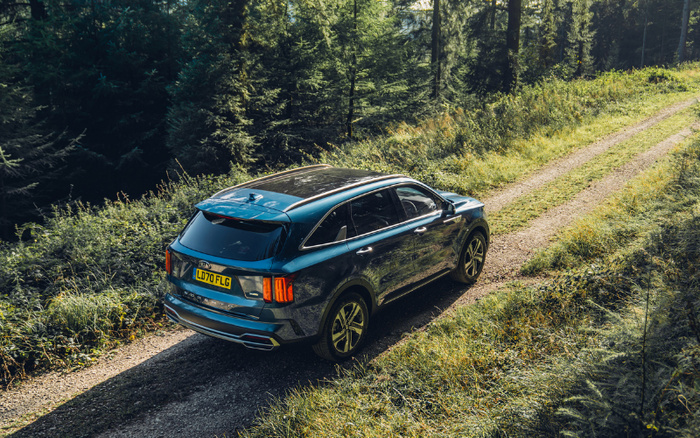 Blue SUV driving on a gravel forest path surrounded by greenery, with the UK number plate LD70 FLG visible on the rear. The image represents used cars or new cars suitable for off-road or rural driving.