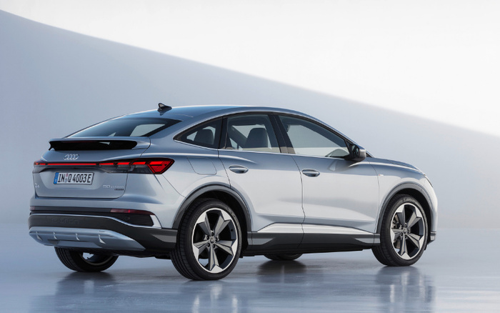 Silver Audi Q4 e-tron SUV electric car parked indoors with license plate IN Q4 003E, viewed from the rear side showing sleek design, black roof spoiler, and five-spoke alloy wheels, ideal for those searching for new cars or used cars with modern electric technology.