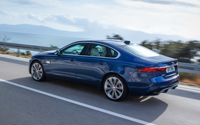 Blue Jaguar XF luxury sedan driving on a coastal road with clear sky and sea in the background, registration plate XFZ 888 visible, representing high-end used cars and new cars.