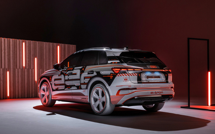 Rear and side view of a black and white Audi e-tron electric SUV with red and orange digital-style patterns on the body, parked in a modern showroom with vertical red neon lights and a wooden panel background, highlighting a sleek design perfect for buyers interested in new cars and used cars.
