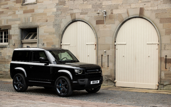Black Land Rover Defender parked on cobblestone street in front of tan stone building with two large cream wooden arched doors and a small window. Vehicle registration plate reads 108 CCM. Scene depicts a modern used car parked near historic architecture, highlighting contrast between used cars and traditional setting.