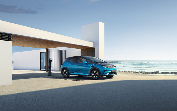 Blue electric car charging at a modern home with minimalist architecture near the seaside, highlighting sustainable new cars technology and eco-friendly transportation options within the used cars and new cars market.