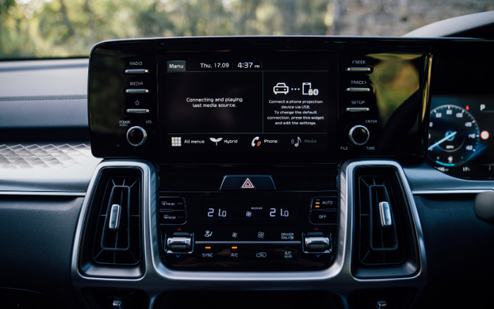 Interior dashboard of a modern car showing the infotainment screen displaying the time 4:37 pm, date Thu, 17.09, and a message about connecting and playing the last media source via USB phone projection. The screen has options for All menus, Hybrid, Phone, and Media. Below, the climate control panel shows dual temperature settings at 21.0 degrees Celsius with SYNC, A/C, and driver and passenger controls. The dashboard features buttons for radio, media, seek, track, setup, and volume control, highlighting features typical in used cars and new cars.