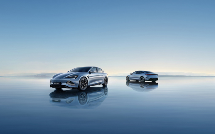 Two sleek, modern electric cars in silver colour displayed on a reflective water surface under a clear blue sky, featuring the BYD Seal model. The image represents new cars with futuristic design, ideal for advertising used cars and new cars in an eco-friendly context.