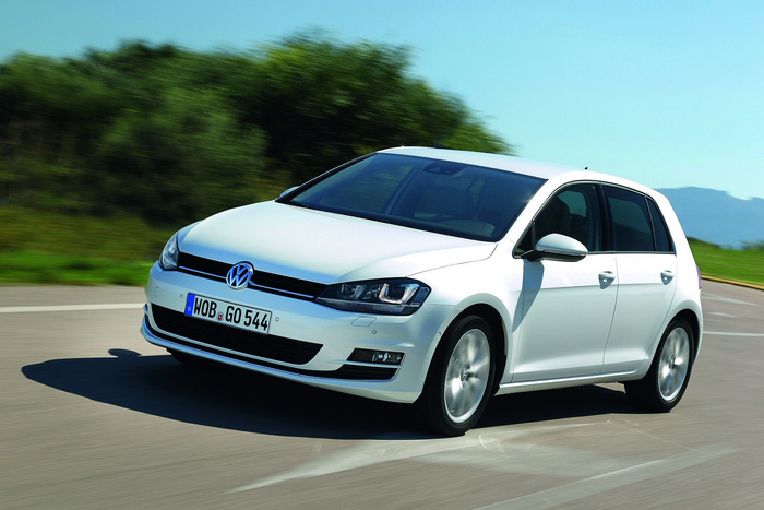 White Volkswagen Golf car driving on a curved road with greenery and hills in the background, featuring a German license plate WOB GO 544, representing used cars and new cars options.