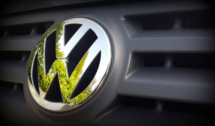 Close-up image of a Volkswagen car grille featuring the chrome VW logo with a reflection of green trees, representing used cars and new cars from Volkswagen.