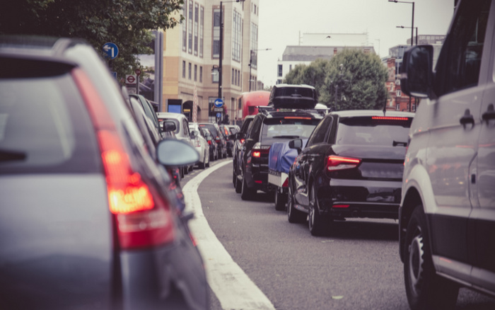 Traffic jam on a city street with multiple vehicles including cars and a white van, surrounded by buildings and trees, illustrating a typical urban scenario relevant to used cars and new cars in busy environments.