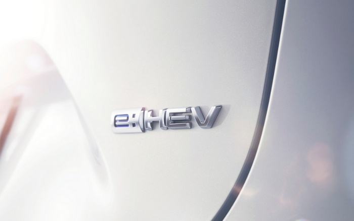 Close-up image of a car badge with the text 'e:HEV' on a shiny light silver or white vehicle surface, depicting a hybrid electric vehicle emblem, relevant for new cars and used cars.